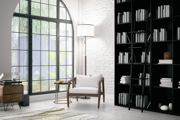 Hình ảnh góc đọc sách bên cửa sổ vòm kính với ghế bành gỗ lót nệm trắng, đèn sàn lớn, cạnh đó là giá sách cao kịch trần