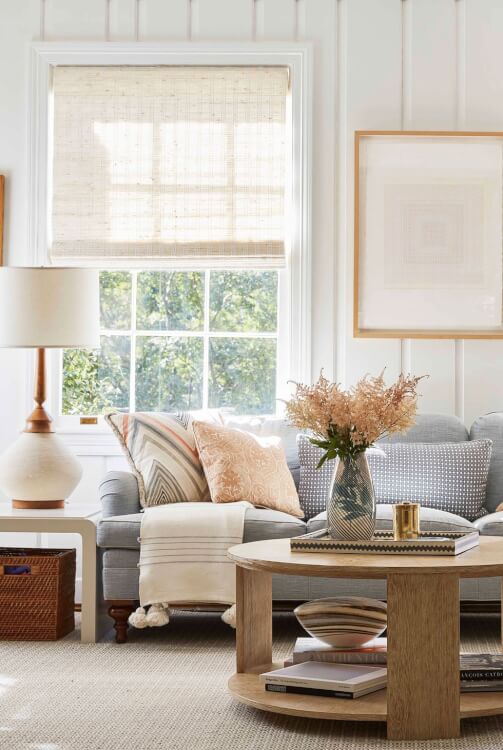 Hình ảnh một góc phòng khách với sofa xám, gối tựa màu sắc, bàn trà gỗ tròn, cửa sổ kính