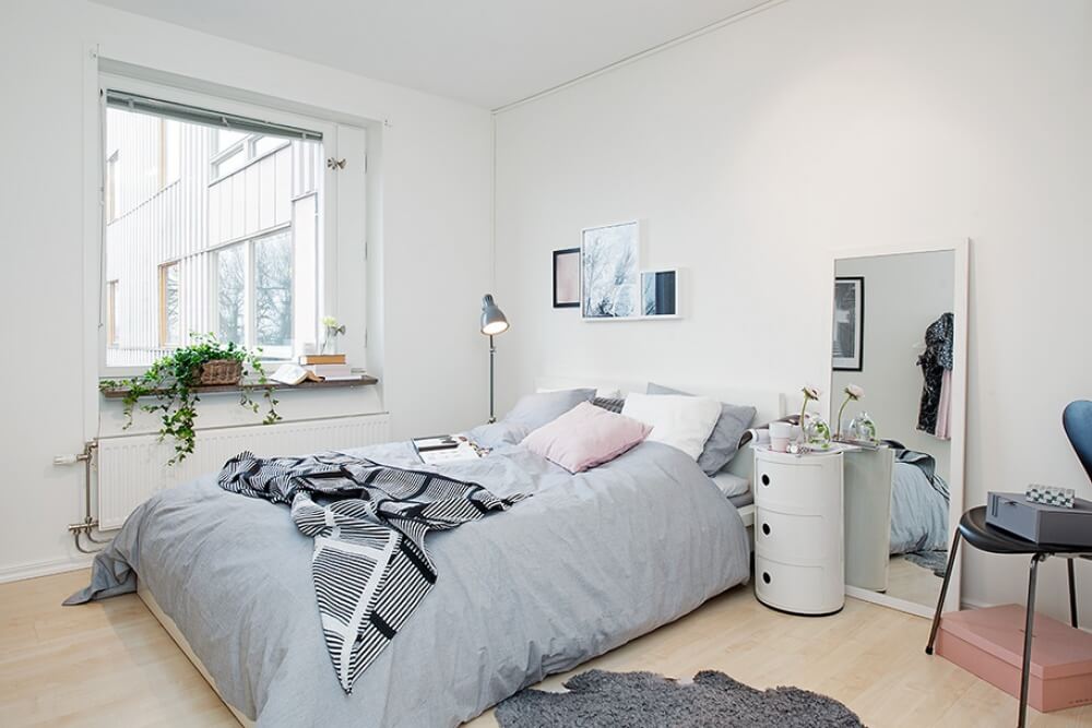 Hình ảnh một phòng ngủ nhỏ với sơn tường màu trắng, cửa sổ kính thoáng sáng, chậu cây xanh tạo điểm nhấn
