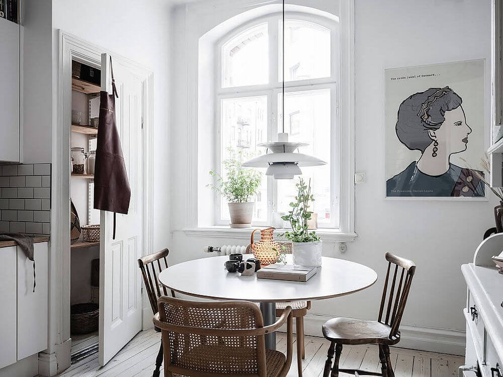 Hình ảnh phòng ăn nhỏ phong cách bắc âu với tông trắng chủ đạo, bàn gỗ tròn, cửa sổ kính trong suốt, tranh tường nghẹ thuật