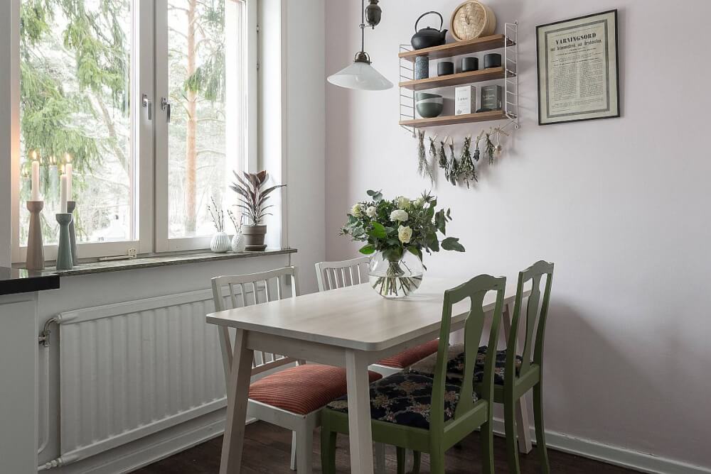 Hình ảnh phòng ăn nhỏ với ghế ngồi màu xanh lá tạo điểm nhấn, cạnh đó là cửa sổ kính thoáng sáng, cây hoa trang trí