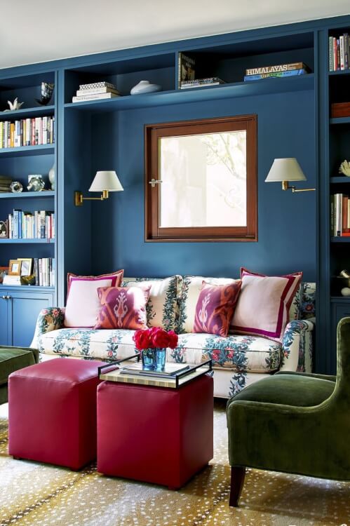 Hình ảnh một góc phòng khách với sofa xanh dương, ghế ottoman đỏ làm bàn trà