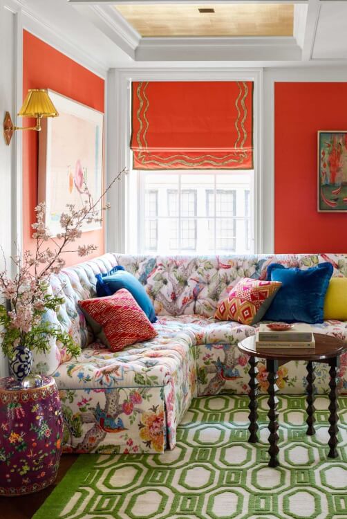 Hình ảnh phòng khách rực rỡ sắc màu với tường sơn màu đỏ cam, sofa bọc vải hoa, cửa sổ kính