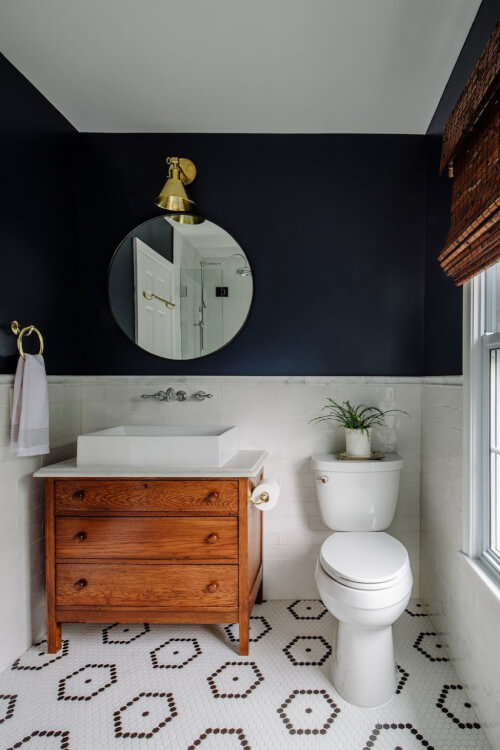 Hình ảnh phòng tắm nhỏ với mảng tường màu xanh navy ấn tượng, gạch lát họa tiết đen trắng, gương tròn, tủ gỗ ngăn kéo