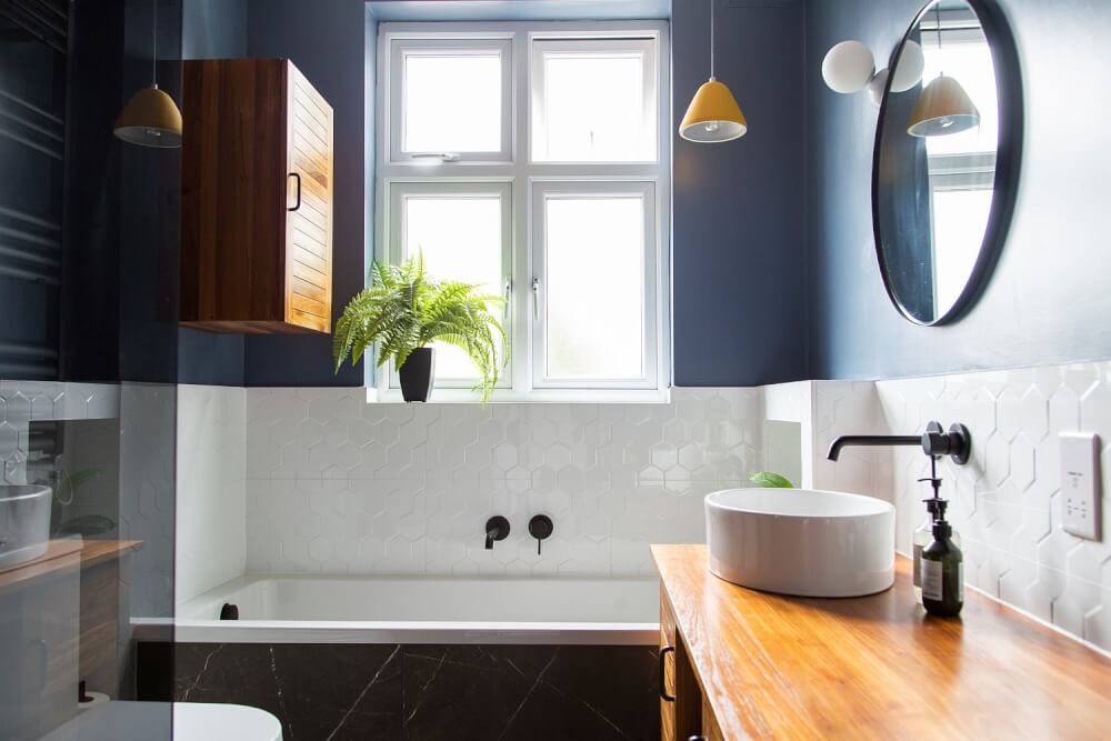 Hình ảnh phòng tắm nhỏ với nửa tường phía trên sơn màu xanh dương, nửa dưới ốp gạch trắng, bàn trang điểm bằng gỗ