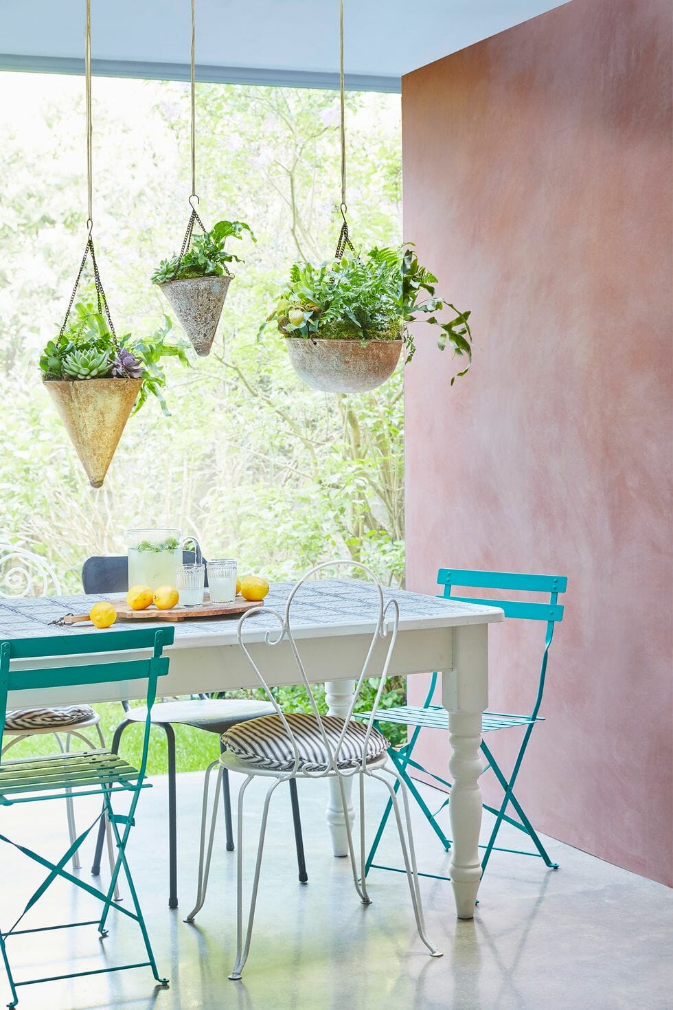 hình ảnh góc thư giãn nơi hiên nhà mùa hè với bức tường màu hồng phấn, ghế xanh ngọc, đèn thả bắt mắt
