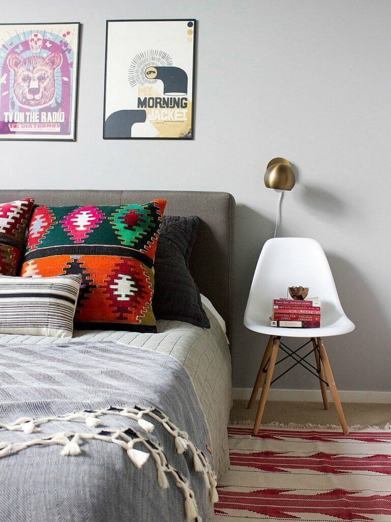 Hình ảnh một góc phòng ngủ mùa hè với ghế đầu giường màu trắng, gối tựa và thảm trải họa tiết màu sắc, tranh treo tường ấn tượng