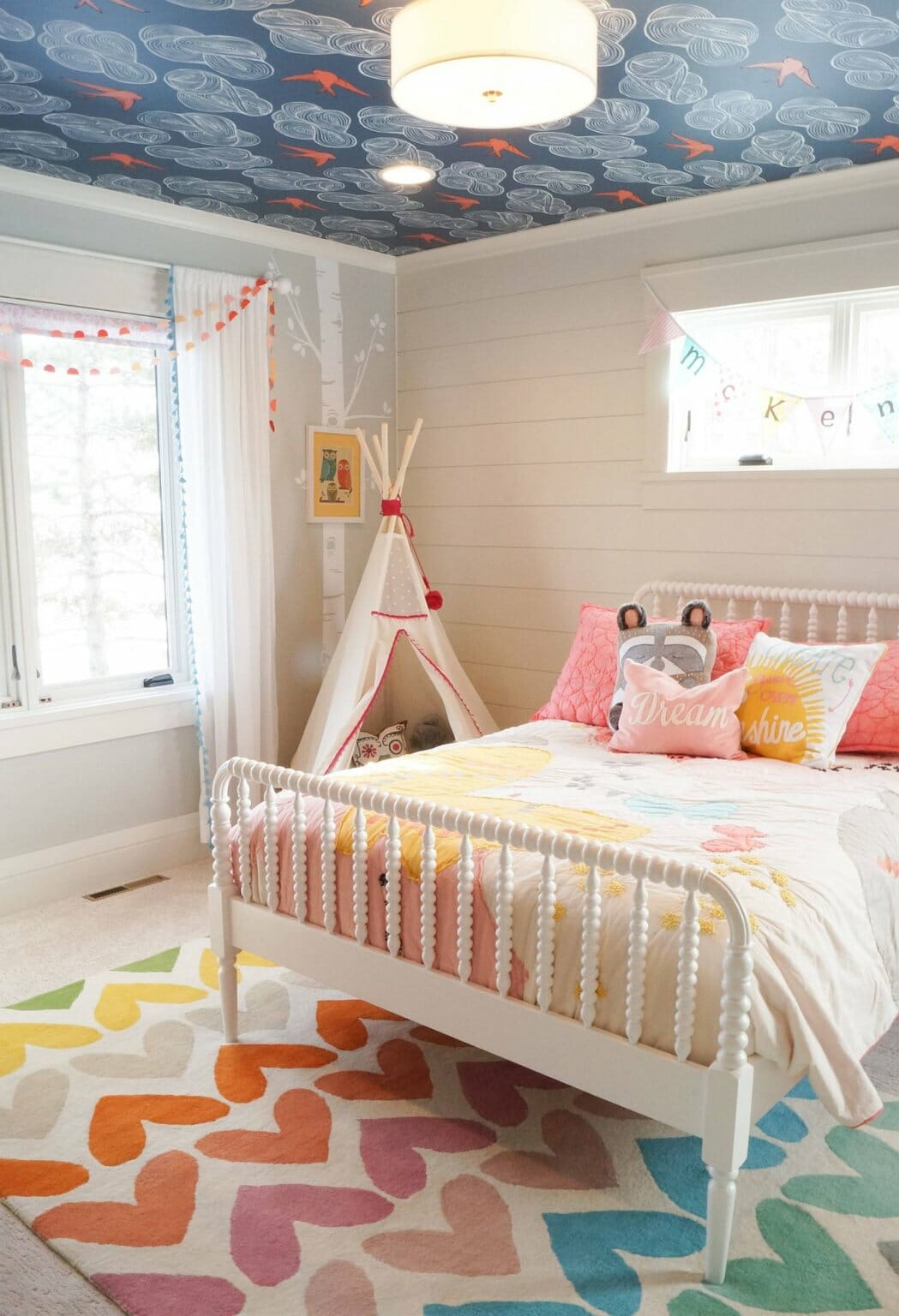 phòng ngủ của bé gái với giường cũi, thảm trải màu sắc, giấy dán trần họa tiết lạ mắt, đèn chùm sang trọng