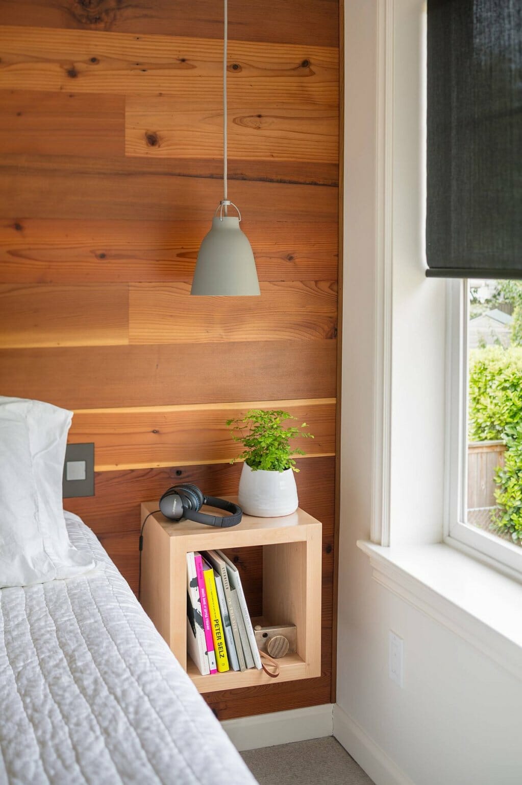 hình ảnh góc phòng ngủ hiện đại với đèn thả màu xám trắng, tường ốp gỗ, kệ sách nhỏ, chậu cây xinh xắn