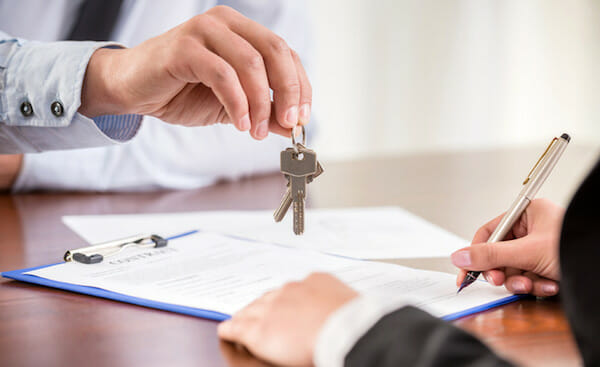 hình ảnh một người đang ký vào hợp đồng, một người cầm chùm chìa khóa trao cho