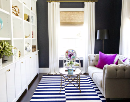 Hình ảnh phòng khách nhỏ với tường sơn đen, giá sách màu trắng cao kịch trần, rèm trắng, ghế sofa cổ điển, thảm trải kẻ sọc